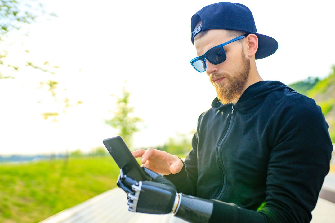 Ein junger Mann mit einem künstlichen Arm bedient ein Smartphone.