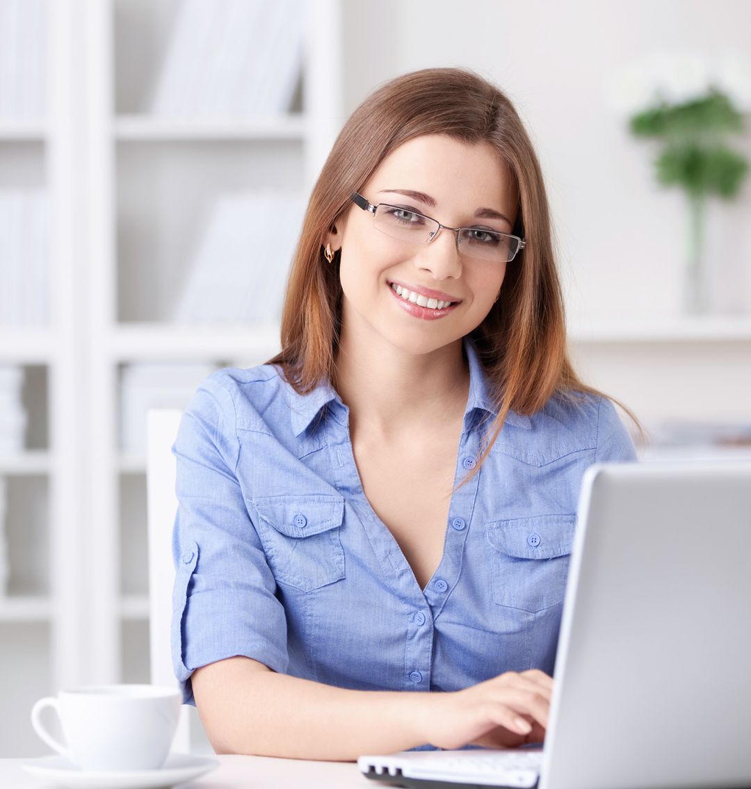 Junge Frau mit Brille, langen Haaren und blauer Bluse sitzt an einem Laptop und tippt.